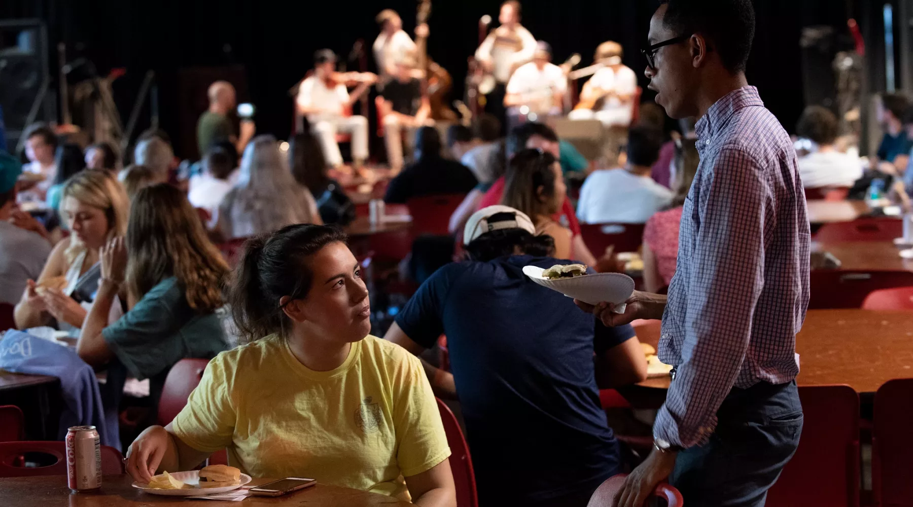 Two students talking at the Red Barn with musicians in the background